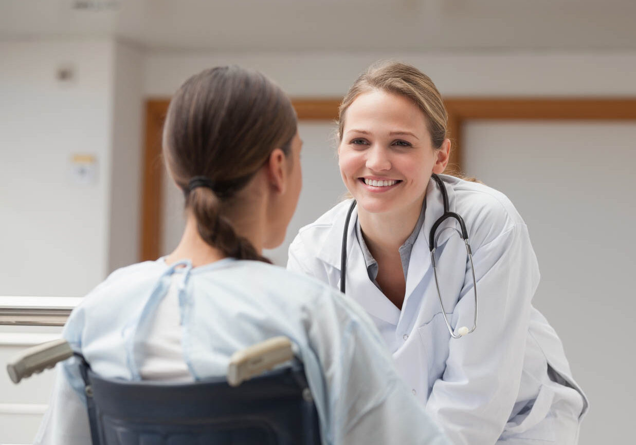 Smiling doctor in front of a patient on a wheelchair in hospital hallway