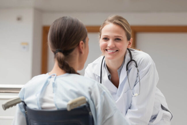 Smiling doctor in front of a patient on a wheelchair in hospital hallway